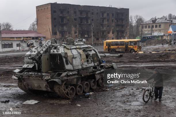 Man pushes his bike through mud and debris past a destroyed Russian tank in front of the central train station that was used as a Russian base on...