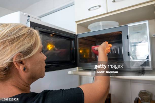 hausfrau stellt einen topf in die mikrowelle - mikrowelle stock-fotos und bilder