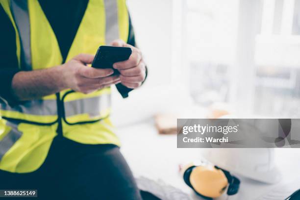 building contractor using his phone to schedule the construction work - protective workwear for manual worker stockfoto's en -beelden