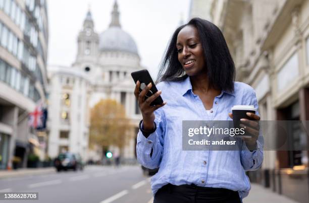 geschäftsfrau trinkt kaffee auf der straße, während sie ihr handy überprüft - business women london stock-fotos und bilder