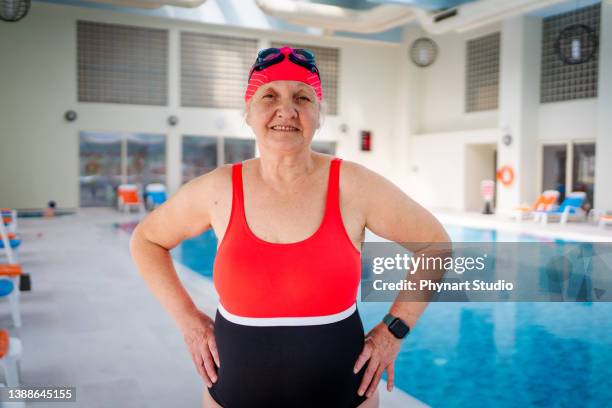 femme âgée active regardant la caméra et souriant après la baignade dans la piscine intérieure - studio portrait swimmer photos et images de collection