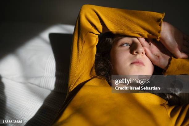 close up view of a lonely young girl looking away to the sunlight coming from the window while lying on bed at home. - teen eye contact photos et images de collection