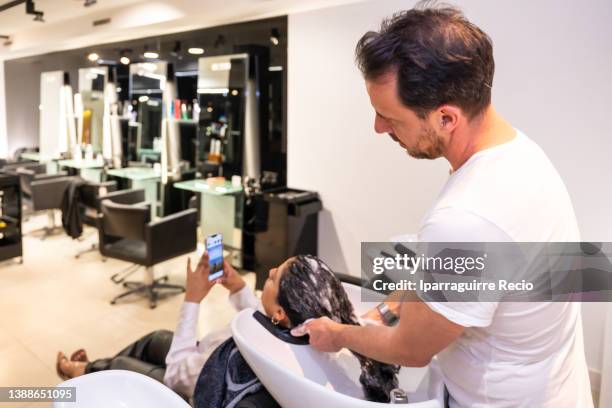 modern and luxury hairdressing salon, a hairdresser cleaning the curly hair of the female client with hot water and shampoo in the barbershop - hair color saloon stock pictures, royalty-free photos & images