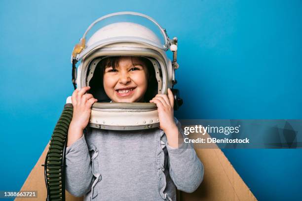 little girl with cardboard wings and astronaut cosmonaut helmet, on blue background. concept of dreams, fly, freedom and creativity. - costume wing stock pictures, royalty-free photos & images