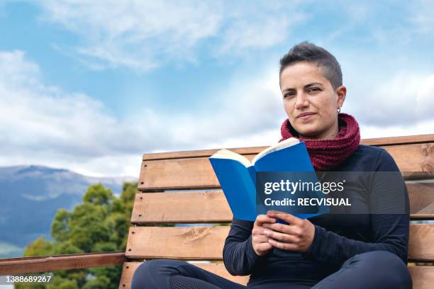 relaxed young woman in a chair reading a book. - bienestar mental stock pictures, royalty-free photos & images