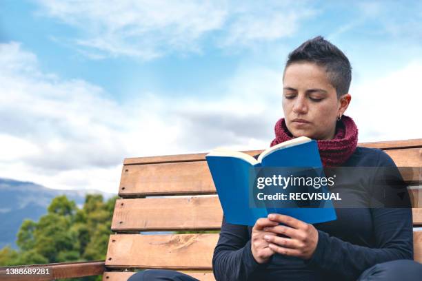 relaxed young woman in a chair reading a book. - bienestar mental stock pictures, royalty-free photos & images