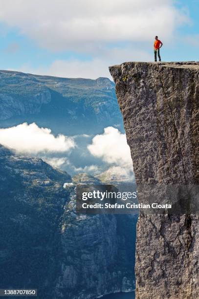 a man sits at the edge of the steep cliff of preikestolen looking at the view above lysefjorden. fjord goes far inland. - preikestolen bildbanksfoton och bilder