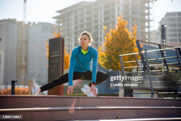 junge sportliche frau, die die beine in einem seitlichen ausfallschritt oben auf der treppe in der nähe eines wohngebiets ausstreckt - athleisure stock-fotos und bilder