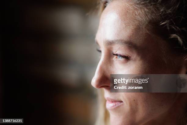 close-up on profile view of woman looking at distance with satisfied expression on her face - casual woman pensive side view stockfoto's en -beelden