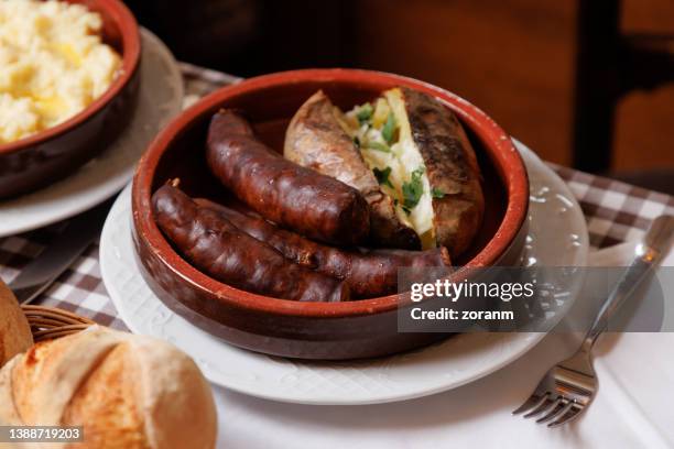 smoked sausages served with baked potato in rustic pottery on restaurant table - jacket potato stock pictures, royalty-free photos & images