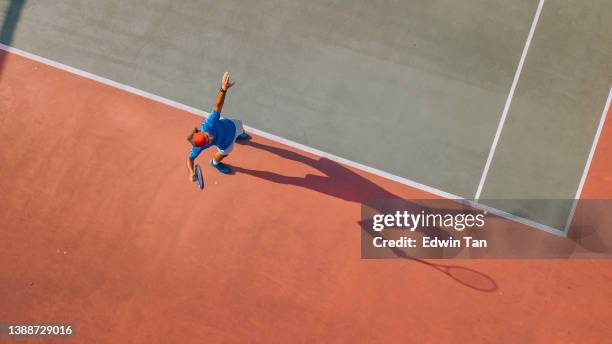 drohnen-blickwinkel asiatischer tennisspieler serviert den ball mit schatten direkt darüber - tennisschläger stock-fotos und bilder