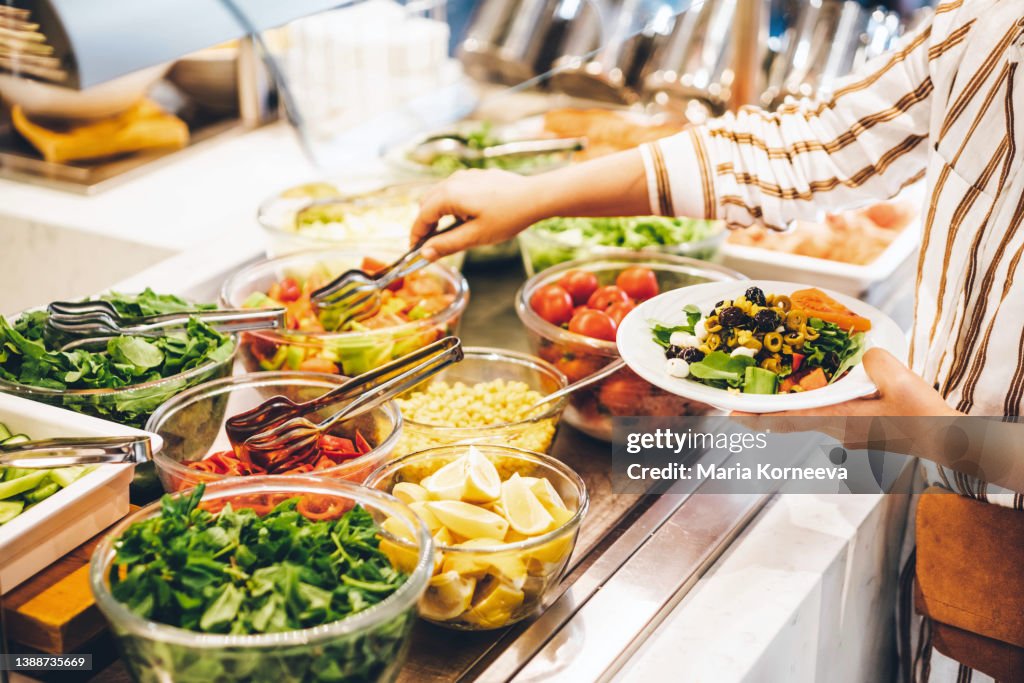 Woman choosing food for breakfast at hotel restaurant. Woman taking food from a buffet line.