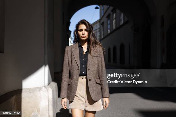 a young girl dressed in a brown coat, black shirt and shorts stares into the camera. - mannequin mode street photos et images de collection