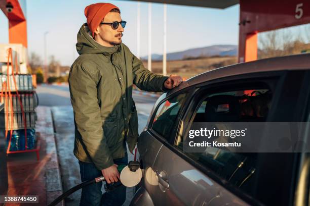 ein mann mit sonnenbrille gießt benzin in sein auto an einer tankstelle - depot stock-fotos und bilder