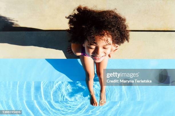 a dark-skinned child sits near the pool and put his feet in the water. dark girl. summer. swimming in the pool. vacation vacation. childhood. pastime. lifestyle. - african american teen stockfoto's en -beelden
