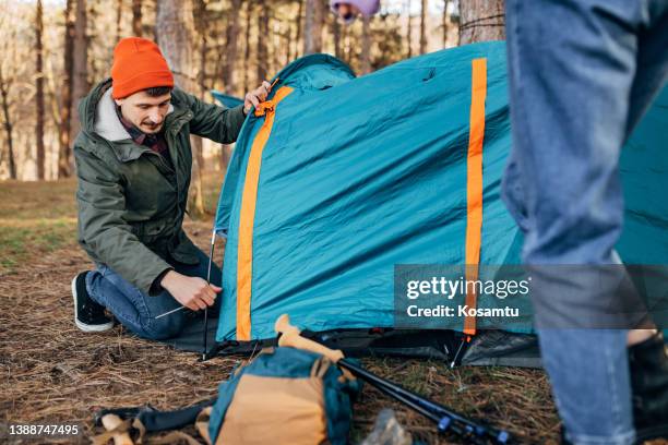 un camper maschio millenario prepara una tenda da campeggio per un pernottamento nella natura - picchetto da tenda foto e immagini stock