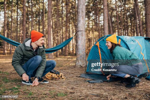 two smiling campers set up a tent in the woods, during a sunny day. - tent stake stock pictures, royalty-free photos & images