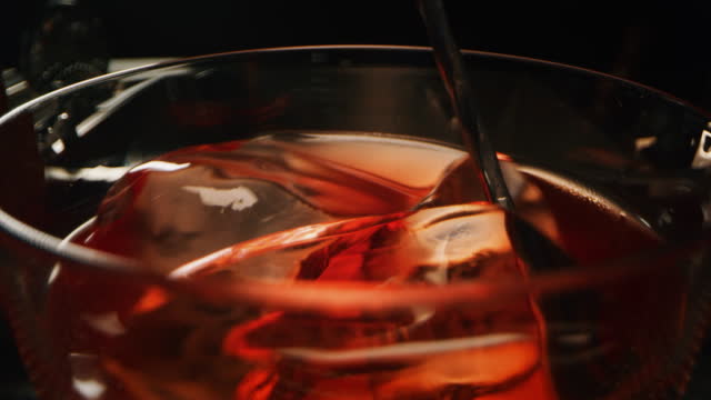 Macro of a professional bartender is preparing an alcoholic cocktail with ice cubes to customers at the bar or disco club.