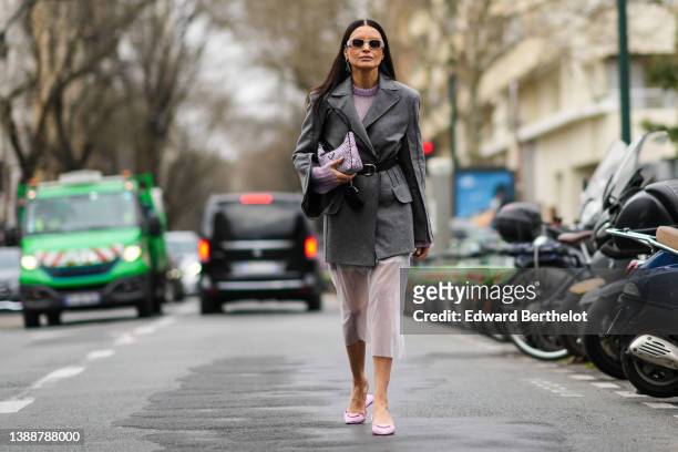 Guest wears beige sunglasses from Prada, a black and silver triangular earring from Prada, a pale purple wool pullover, a gray belt coat, a black...