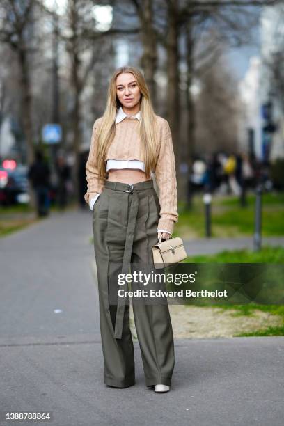 Guest wears a white cropped / ripped shirt from Miu Miu, a beige braided wool cropped pullover from Miu Miu, high waist khaki belted palazzo pants, a...