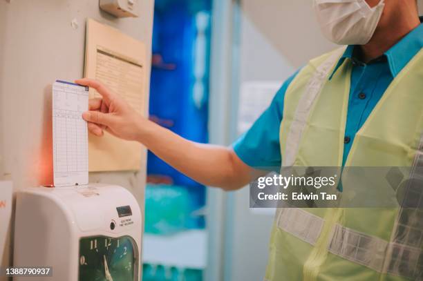 close up asian chinese blue collar worker clock in with time card punching in the morning - clocking in machine stock pictures, royalty-free photos & images