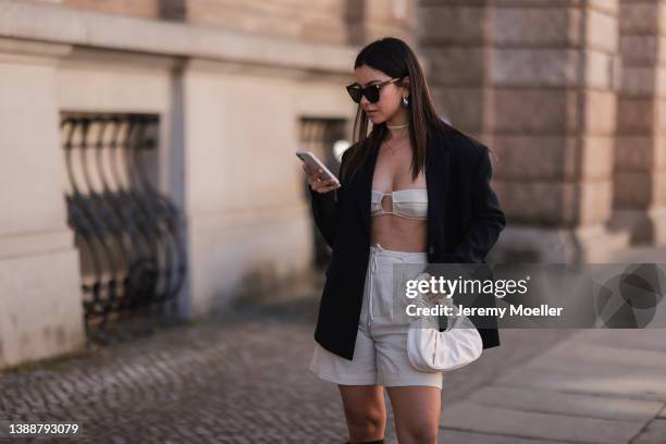 Bella Ema seen wearing a black sunglasses, silver earrings, a black oversize LeGer blazer, a creme satin crop top from LeGer, a creme linen shorts...