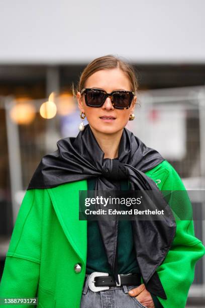 Guest wears sunglasses, gold with large pearl pendant earrings, a black silk scarf, a neon green long oversized coat, a black shiny leather belt,...