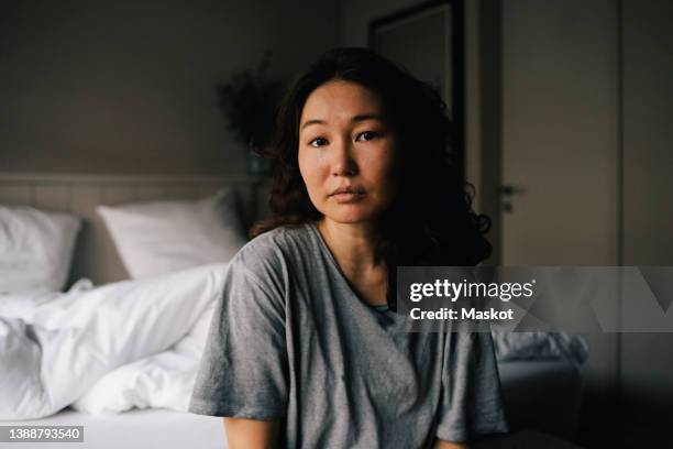 portrait of sad woman with mental health illness sitting in bedroom at home - looking at camera serious stock pictures, royalty-free photos & images