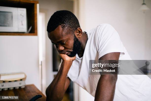 thoughtful lonely man with hand on chin leaning in kitchen at home - eating disorder stock pictures, royalty-free photos & images