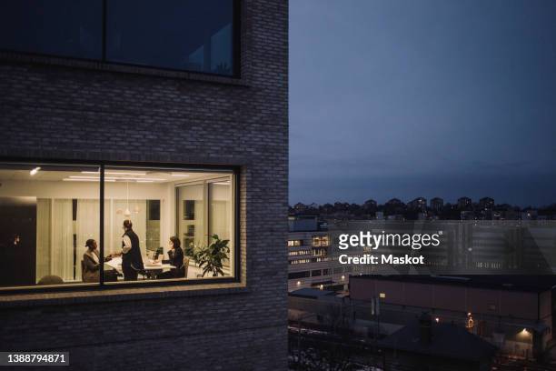 multiracial female colleagues working late seen through window of work place - job centre stock pictures, royalty-free photos & images