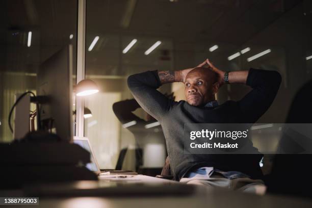 mature businessman with hands behind head working late in office at night - hands behind head stock pictures, royalty-free photos & images