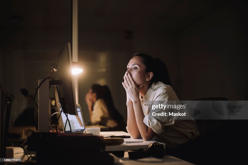 Businesswoman with hands covering mouth working on computer in office