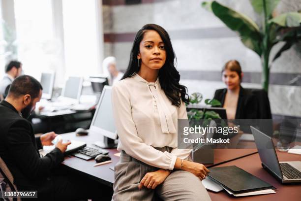 portrait of confident businesswoman sitting on desk in law office - incidental people stock pictures, royalty-free photos & images