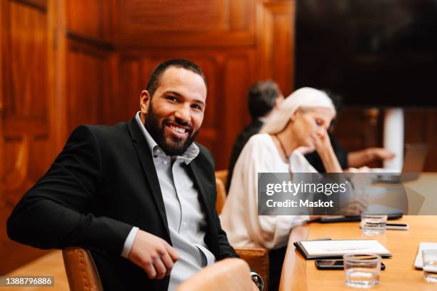 portrait of smiling businessman sitting at conference table in board room during meeting - legal occupation stock pictures, royalty-free photos & images