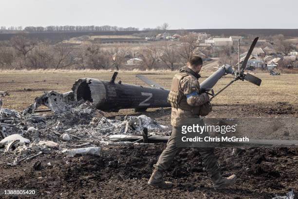 Member of the Ukrainian military walks past the remains of a downed Russian helicopter on March 31, 2022 in Malaya Rohan, Ukraine. A Ukrainian...