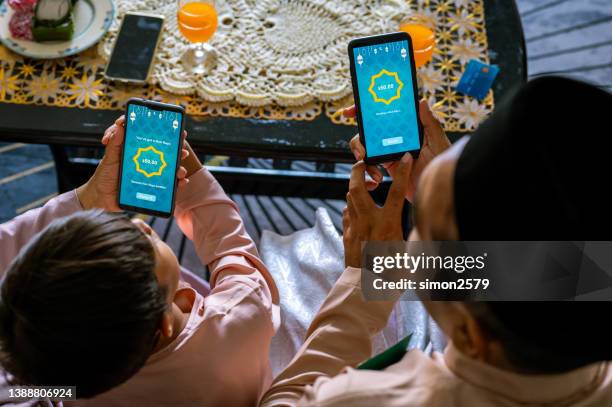 young asian boy being presented with a digital gift of e-money from his father as part of the islamic celebration of hari raya aidilfitri (eid al-fitr). - raya decoration stock pictures, royalty-free photos & images