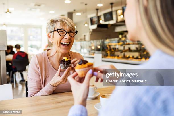 smiling women talking over cupcake and coffee - mature woman daughter stock pictures, royalty-free photos & images