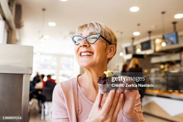 senior woman eating cupcake - person holding cupcake stock pictures, royalty-free photos & images