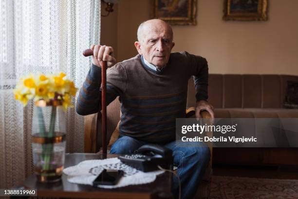 senior man having back pain issues when getting from an armchair - standing on chair stockfoto's en -beelden