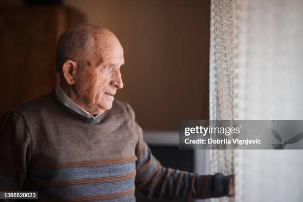 elderly man removing curtains and looking through the window - worry free stock pictures, royalty-free photos & images