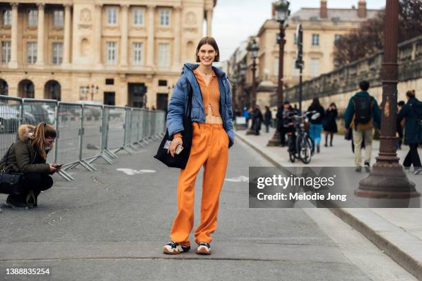 Dutch model Merel Roggeveen wears a cropped blue puffer jacket, orange cropped front zip zebra print cardigan, orange trousers, and chunky black and...