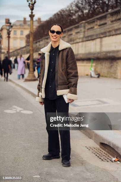 French-American model Sophie Koella wears black sunglasses, a brown shearling jacket, black shirt, black pants, and black boots after the Dior show...