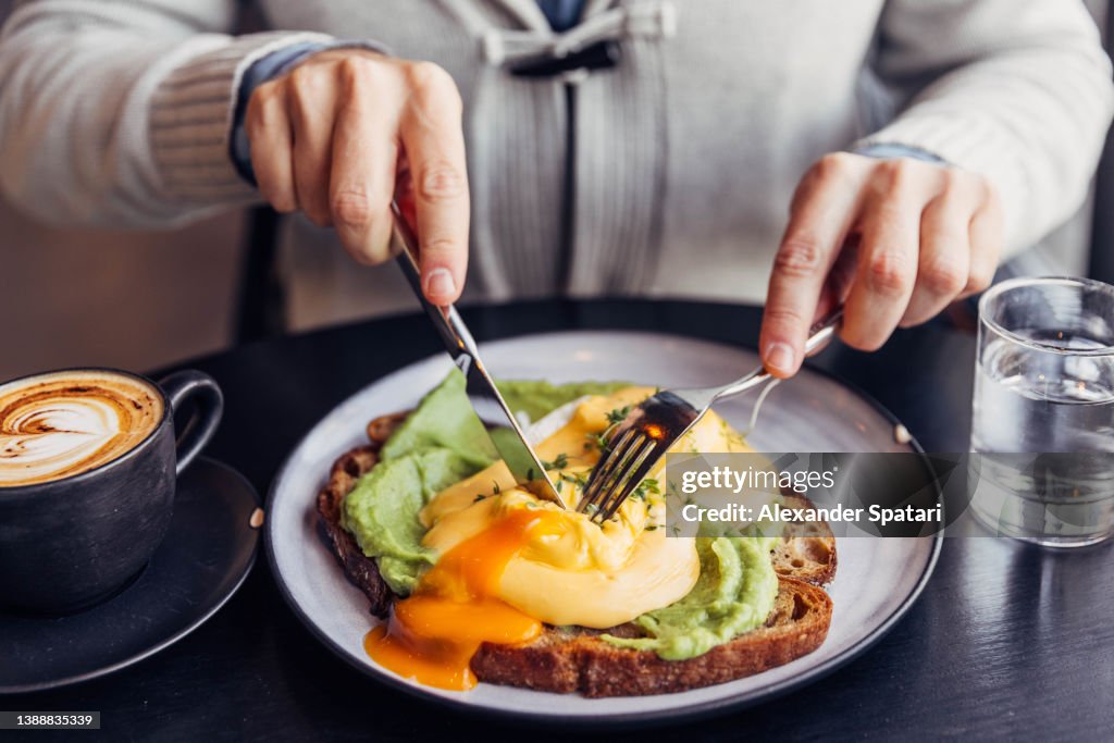 Close-up of a man eating avocado toast with poached egg for breakfast at a cafe