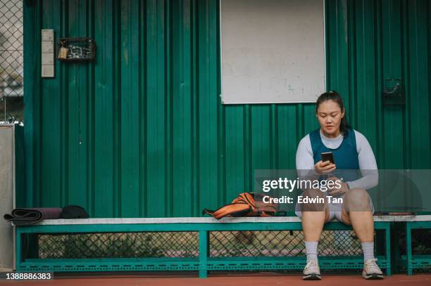 asian chinese mid adult woman sitting on bench in tennis court checking on her smart phone tracking her heartbeat rate after the game - forward athlete stock pictures, royalty-free photos & images