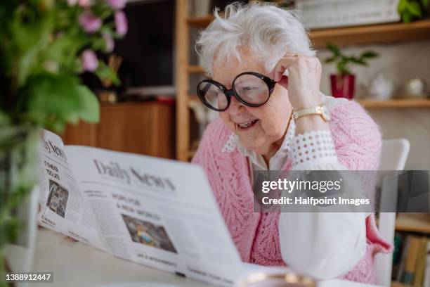 senior woman with funny glasses reading newspaper at home. - magazines on table stock pictures, royalty-free photos & images
