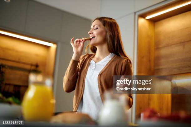 happy woman enjoying while eating cookie at home. - biscuits imagens e fotografias de stock