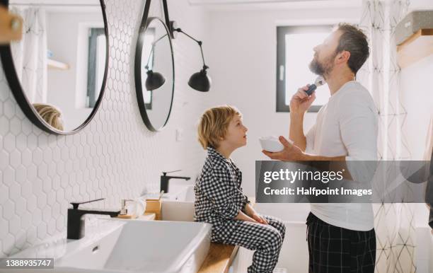 father with small child indoors in bathroom in the morning at home, shaving. - barbear imagens e fotografias de stock