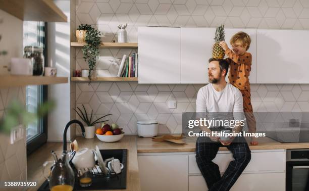 father sitting on kitchen counter with his little son and having morning coffee. - family small kitchen stock pictures, royalty-free photos & images