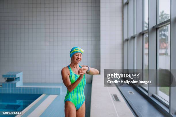 senior woman swimmer preparing for swim indoors in public swimming pool. - cuffia da nuoto foto e immagini stock