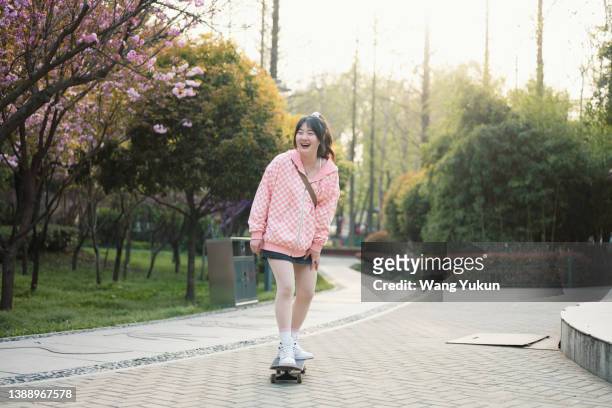 frontal full body shot of young woman riding skateboard in park - full frontal female stock pictures, royalty-free photos & images